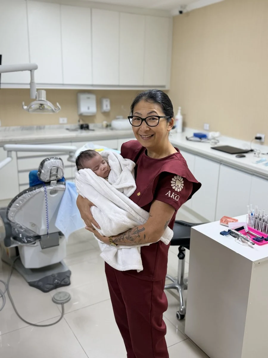Dra. Elza Nara sorrindo e segurando um bebê no consultório da AKO